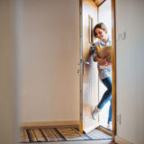 A young woman with groceries in paper shopping bag walking in through front door at home. Copy space.